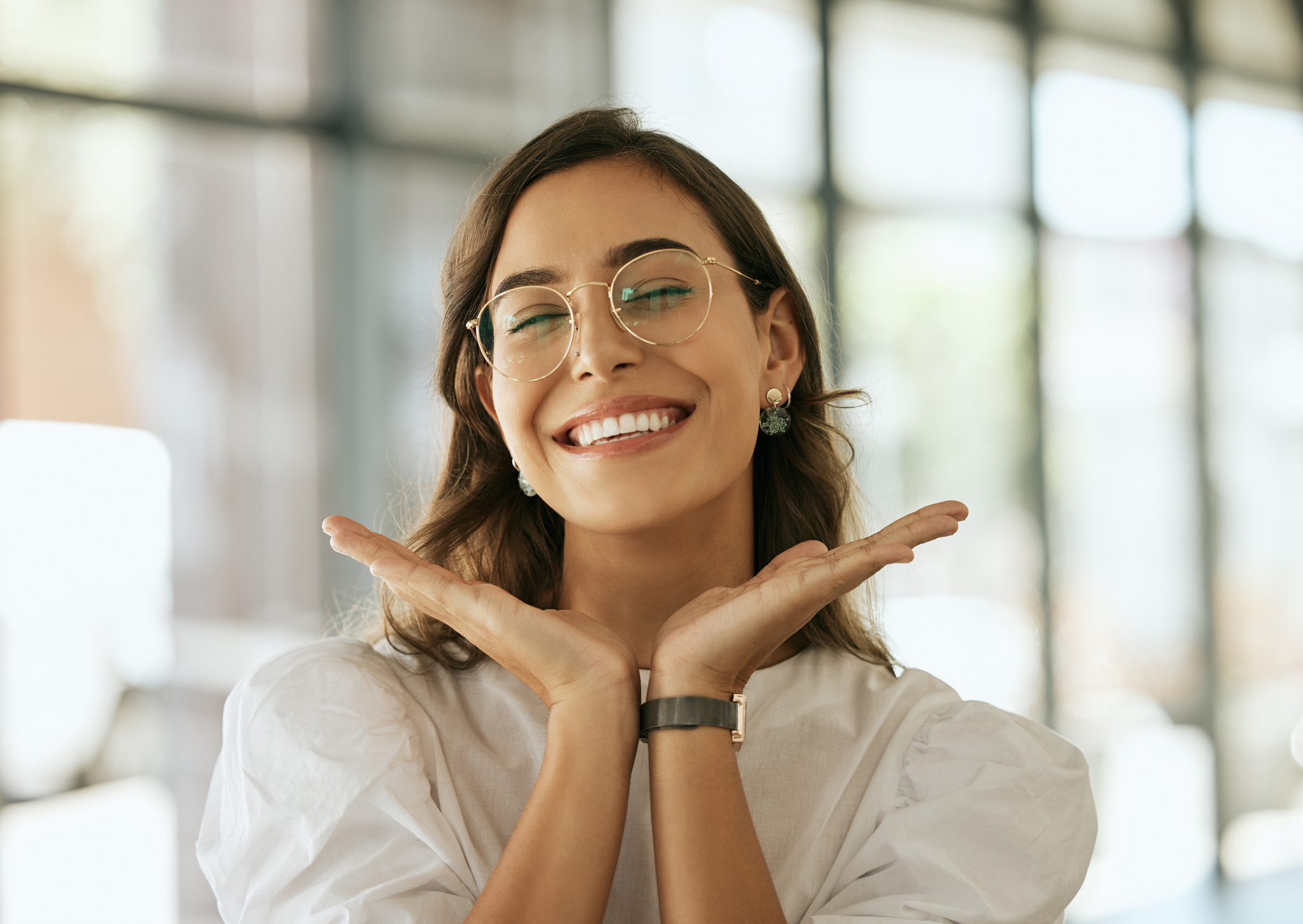 Cheerful business woman with glasses posing with her hands under her face showing her smile in an office. Playful hispanic female entrepreneur looking happy and excited at workplace Professional Teeth Whitening in Summerville SC